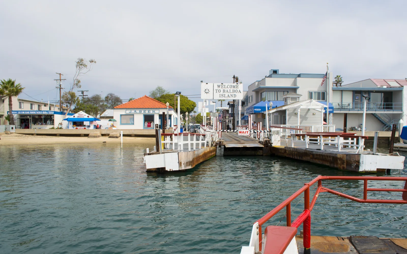 Balboa Island Ferry crossing Newport Harbor, with residential homes and sailboats in the background